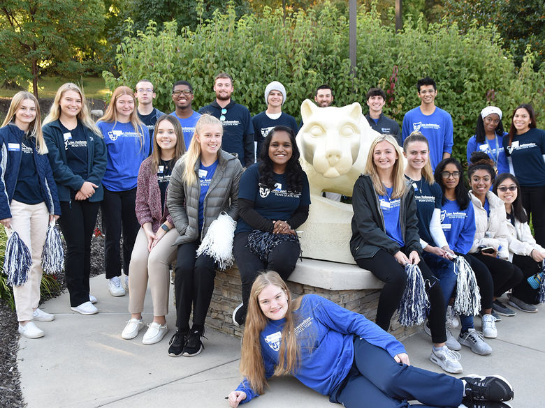 Students involved in the Lion Ambassadors program sitting and standing around the Nittany Lion statue outside the John J. Romano Administration Building.