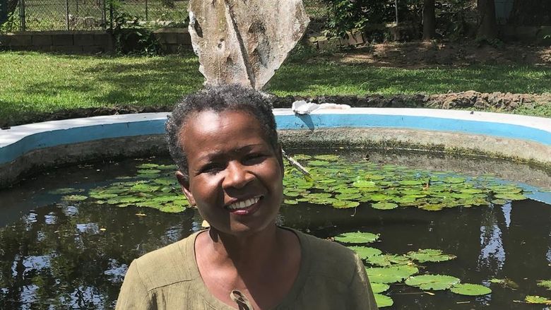 African American woman with short hair standing in front of a fountain of water and lily pads..