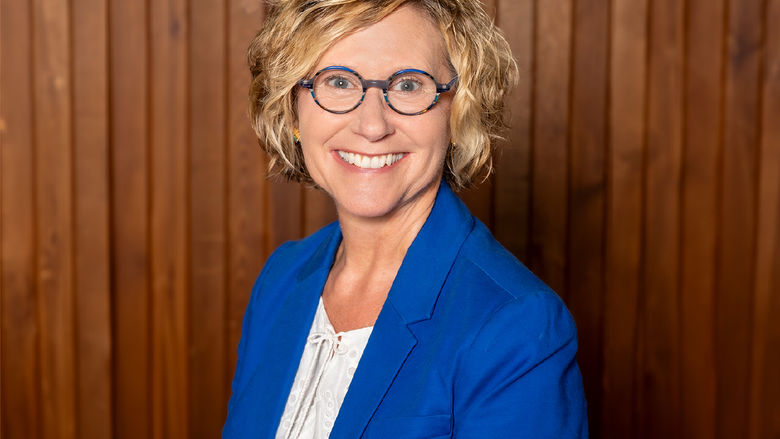 Headshot of adult female with blonde hair and wearing glasses, dress in a suit