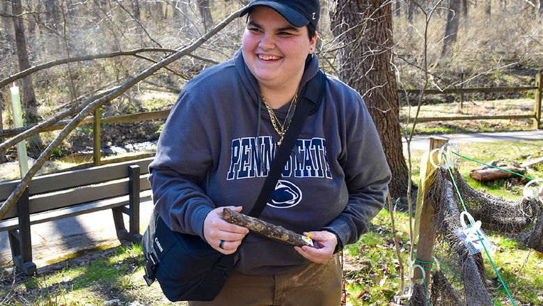 STudent wearing a Penn State hat and sweat holds a lichen sample/