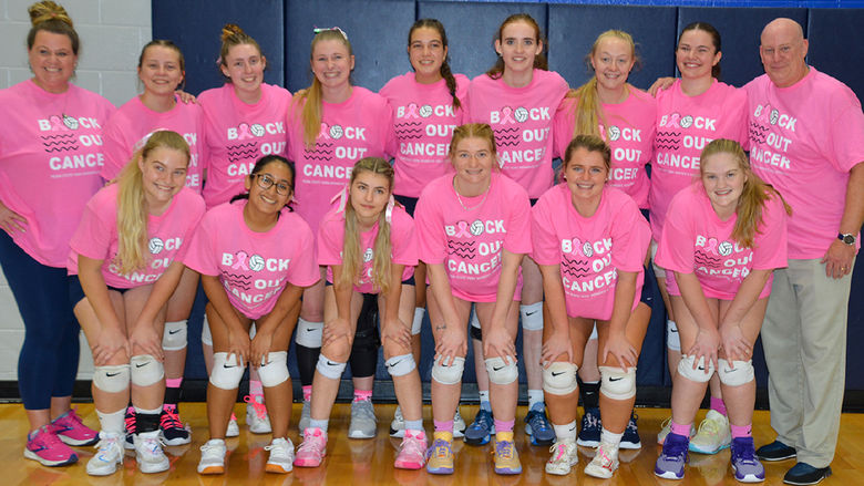 Two adults, female and male, along with thirteen female volleyball players wearing pink T-shirts