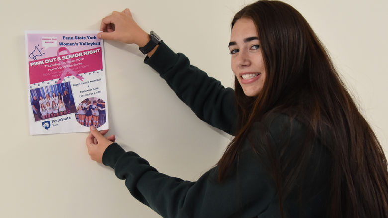 Young woman with long dark hair hanging a poster on the wall