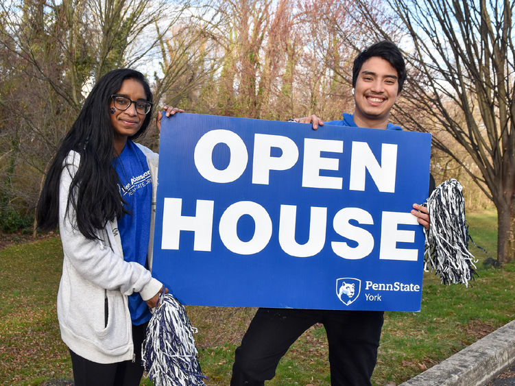 female and male student holding a blue and white open house sign.