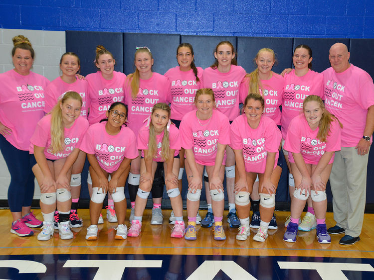 Two adults, female and male, along with thirteen female volleyball players wearing pink T-shirts