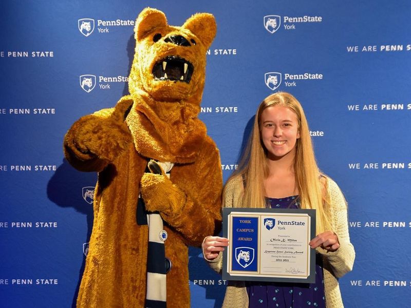 The Nittany Lion mascot standing next to a female student who is holding a certificate.