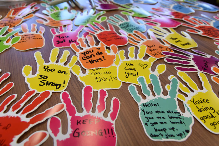 Colorful paper handprints spread on a table with messages of hope written on them.