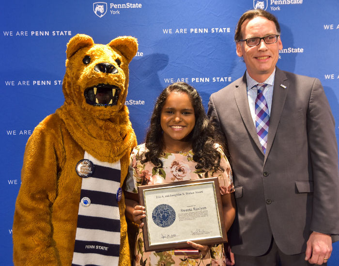 Person in Nittany Lion suit with female award recipient and male presenter at awards program.
