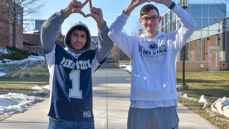 Two male students wearing Penn State attire and forming diamons with their hands