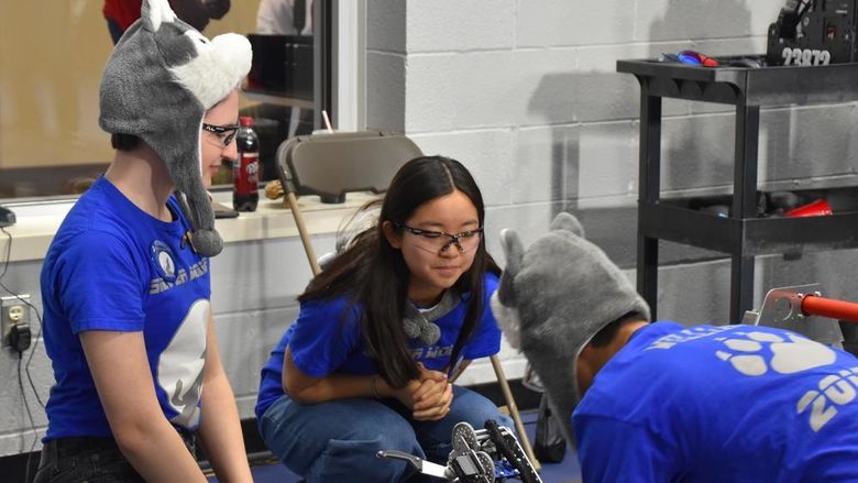 Three students work on a robot, one is wearing a wolf hat