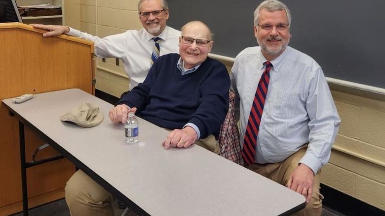 Three men in a classroom, smiling at the camera.