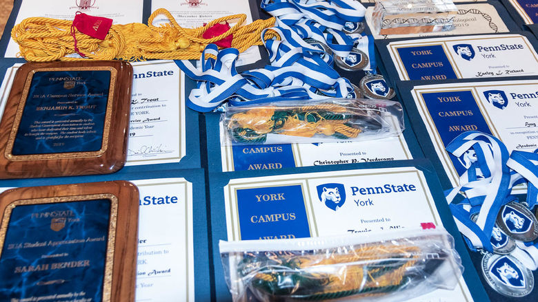 Award plaques, certificates and medals spread across a table at Penn State York. 