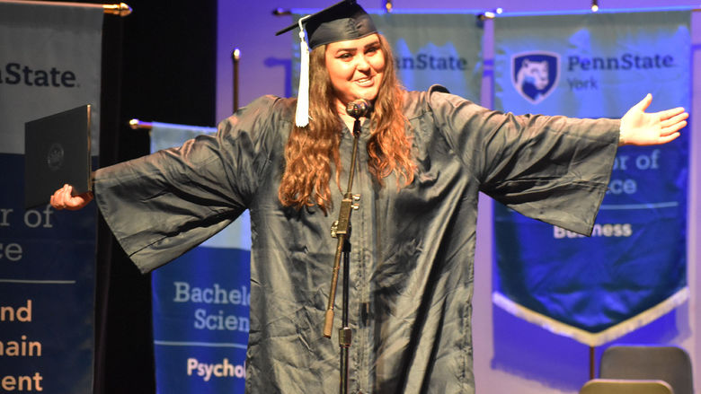 Female student in graduation cap and gown speaking at microphone