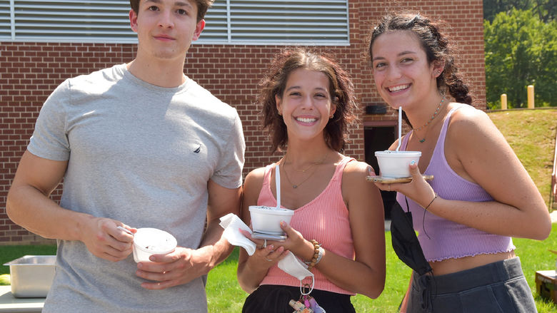 Young male and two females enjoying ice cream outside.