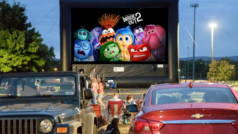 Cars face a large inflatable movie screen for a drive-in movie.