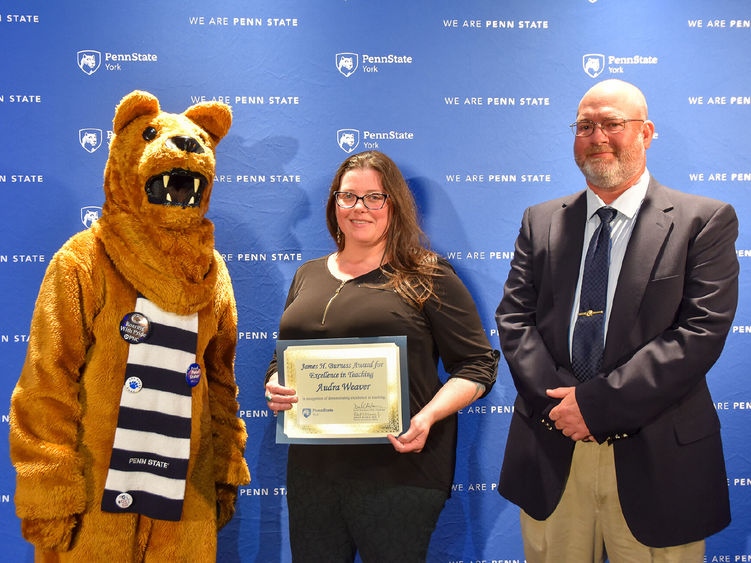 Nittany Lion character stands with female and male faculty members receiving an award