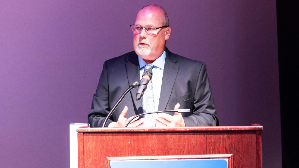 Male person professionally dressed who is speaking at a Penn State York podium. 