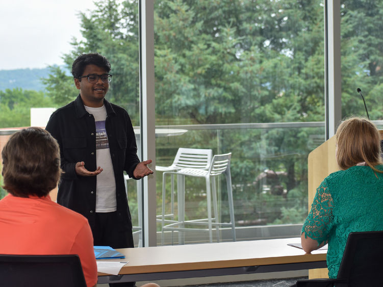 Young man standing in the front of a table presentaing to a male and female