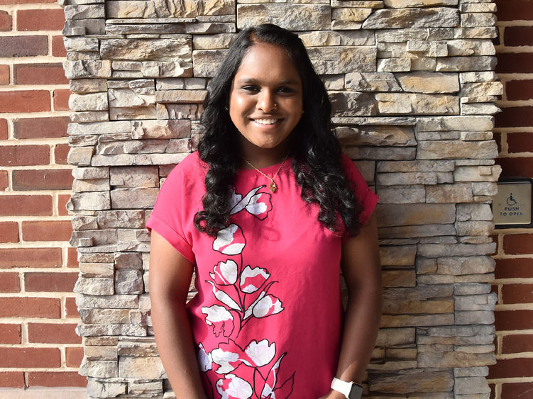 A person wearing a hot pink flowered top, standing against a rock wall.