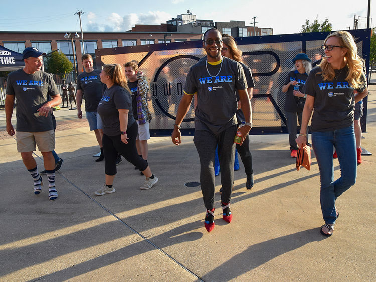 Group of men and women, wearing Penn state York T-shirts, walk wearing high-heeled shoes