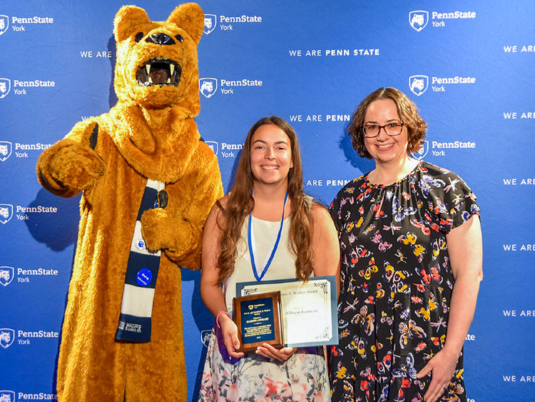 Nittany Lion with female student and female faculty member displaying an award.