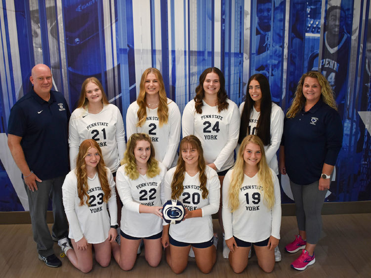 Eight femal volleyball players, dressed in uniform,  and a male and female coach.